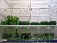 Multiple shelves showing stacks of green depression glass plates, bowls, decanter, candle holders arranged on white wire shelving.