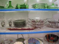 Glassware items on white shelves showing plates, footed bowls, platters, and candlestick holders with fruit decorations