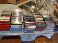 Wide shot of multiple boxes containing numerous music CDs stacked in rows on a kitchen counter.