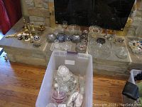 Wide shot showing assortment of glass bowls, candle holders, salt and pepper shakers, napkin holder, butter dish, and decorative items arranged on a hearth.