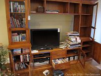 Wooden entertainment cabinet with shelves and drawers occupied by books, DVDs, electronic devices, and stacked books.