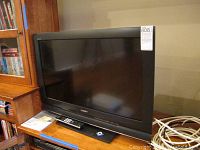 Front view of the Sony 32-inch flat screen TV on a wooden surface with remote and manual nearby