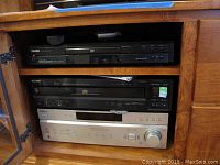 Electronic components inside a wooden cabinet: Toshiba DVD player on top shelf, Sony 5-disc CD player and silver Sony AV receiver below.