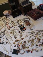 Full display of assorted costume jewelry spread on table including necklaces, earrings, brooches, and boxes grouped behind
