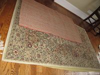 Photo of two rugs layered showing floral border pattern and checkered pattern rug on top.