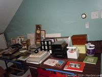 Wide angle shot of table displaying assorted picture frames, baskets, boxes, and a ceramic mug, showing condition and quantity.