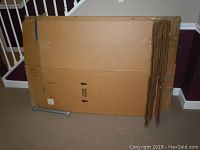 Stacked flattened large cardboard wardrobe boxes with one silver plastic base piece on floor