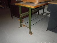 Side view showing green metal frame and wood top of the work bench on concrete floor.