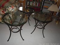 Three oval accent tables with black iron bases and clear glass tops viewed together on floor near floral couch.