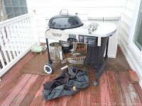 Weber charcoal grill on deck with dome lid, side tray, under-shelf, and black grill cover on floor