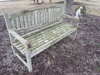 Front angled view of teak wood bench showing lichen growth on seat and backrest, armrests and legs weathered with some erosion.