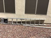 Side view of a 10 foot aluminum extension ladder resting on rocky ground showing general length and condition.