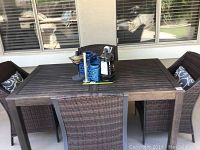 Full view of dark brown wooden rectangular outdoor table with slatted top, four chairs around it, located outdoors near window.