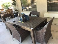 Four wicker and metal outdoor arm chairs around a wooden table on a covered patio, showing overall set and condition.