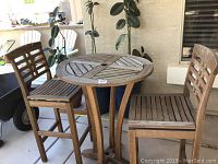 Round wooden bistro table with two wooden bistro chairs on patio, showing general condition.
