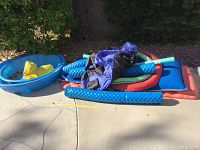 Photo showing two blue inflatable wading pools stacked with a yellow duck float inside the smaller pool and various pool noodles and flat pool floats piled beside.