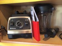 Shelf overview showing blender base, container with lid, tamper, and manual binder
