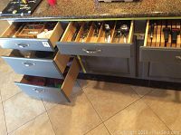 Open kitchen drawers showing organized flatware in trays including forks, spoons, and knives.