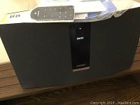 Front view of black Bose SoundTouch 30 speaker with digital display showing time and Wi-Fi icon, remote and manuals on top