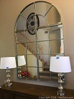 Full view of three-panel mirror mounted on wall above console table with lamps