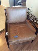 Front view showing the padded brown leather seat and backrest on dark wood frame with armrests.