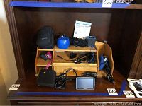 Overview of all items including GPS units, camera, Fitbit, chargers, and accessories on wooden shelf.
