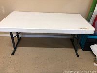 Front view of the white plastic folding table showing rectangular top and black legs.