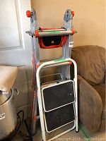 Little Giant folding ladder and white folding step stool leaning against a couch and wall.