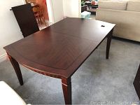 Full view of the dining table showing dark wood grain surface with decorative edging and four legs.