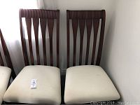 Front view of four wooden dining room chairs with cream fabric seats.