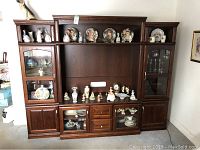 Front view of the complete wooden wall unit TV cabinet displaying various decorative figurines and plates on glass shelves and wooden shelves.