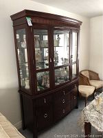 Full front view of wooden buffet and hutch with glass doors showing internal display items, curved top molding, and silver hardware.