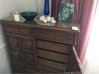 Overall view of the wooden tall dresser with two small top drawers, cupboard with three pullout drawers inside, and three large drawers below, topped with glass panel.