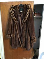 Full view of brown faux fur coat with ruffled collar and cuffs hanging on door showing length and drape