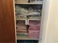 Folded bed linens and towels on shelves inside a closet, showing patterns and colors