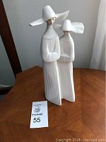 Porcelain figurine of two nuns in white pleated habits with distinctive large white hats on a wooden surface.