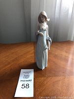 Front view of the Lladro figurine on a wooden table, showing the girl in a light blue evening dress, about 8 inches tall.