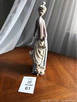 Full view of the Lladro figurine showing the woman standing with her umbrella and the dog at her feet on a wooden surface.