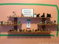 Full view of wall-mounted wooden shelf displaying various animal figurines arranged on three tiers under a framed message.
