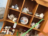 Full view of wooden cubby shelf filled with various teapots, salt and pepper shakers, cups, saucers, and collector plate.