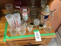 Wide shot showing the full collection of assorted beer stein, beer boot, decanters and assorted drinkware on the wooden surface