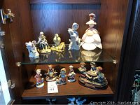 Shelf with multiple figurines showing variety including a woman in ball gown, a hunting boy, smaller child figurines and animals