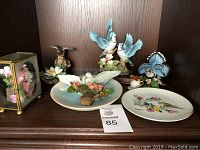 Overview of all items on shelf, showing various bird figurines, decorative plate and glass floral case