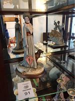 Figurine displayed in glass cabinet showing full view of lady and dog.