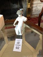 Front angle of Lladro porcelain girl figurine in white dress on glass table.