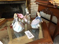 Three Lladro umbrella girl figurines displayed on glass table