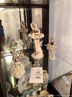 Photo showing four lady figurines including a larger ballerina in white tutu and three smaller dancing girls in detailed dresses, displayed in glass cabinet.