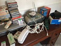 View of Sony VHS/DVD player with remote, Sony Dream Machine CD player, Polaroid camera, panoramic camera, cables, and additional electronics on wooden surface.