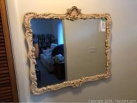 Mirror hanging on wall showing ornate cream frame and reflections of the room, clear view of mirror's size and style.