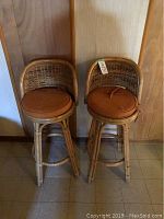 Two wicker bar stools together against a wall, showing overall condition and design.